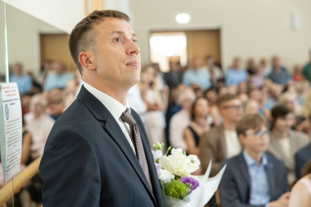 Mees ülikonnas lillekimbuga, taustal täis saal